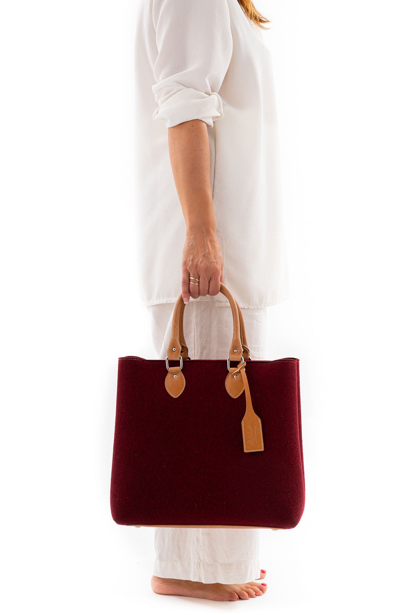 Merino wool felt in 3mm thickness. Vegan leather handles made from organic materials. Detachable Vegan leather shoulder strap with snap hooks. 2 inside pockets. Measurements approx.: 30cm H 33cm W 15cm D/ 11,81 H 12,99” W 5,90” D. Handles drop: 14,5 cm / 5,70”. Pendant plate with Lefrac logo.