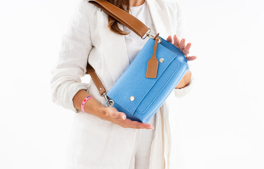 GREGOR Light Blue Beltbag: Compact yet spacious, made from durable 3mm merino wool felt with vegan leather. Features two external pockets for large phones, a smaller internal pocket, and a secure flap with magnetic buttons. Adjustable strap for versatile wear. Handmade in Italy. Includes dust bag. - Lefrac