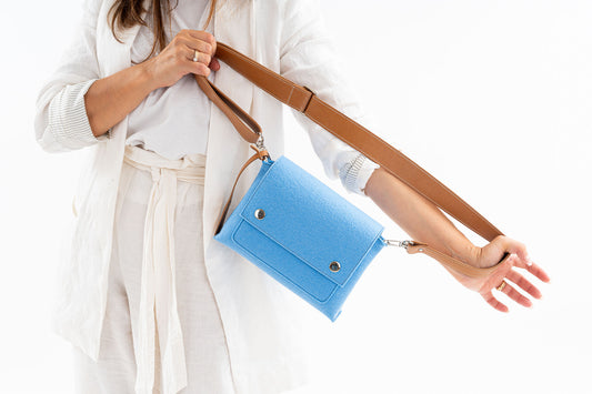 JOY Light Blue Crossbody Bag: Small, ergonomic, and stylish with three pockets (2 external, 1 internal) for organizing essentials. Features an adjustable vegan leather strap, flap closure with magnetic buttons, and a Lefrac logo pendant. Handmade in Italy, includes a dust bag.