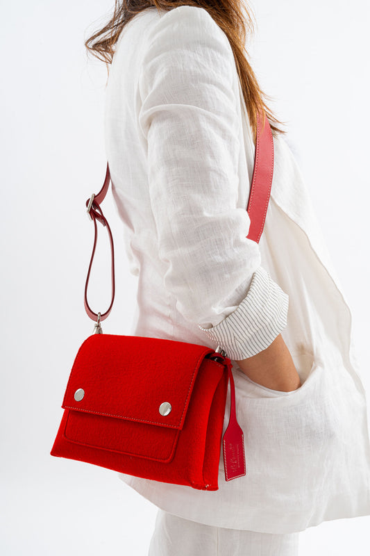 JOY Red Crossbody Bag: Stylish and practical with a comfortable design. Features vibrant colors, three pockets (2 external, 1 internal), adjustable vegan leather strap, flap closure with magnetic buttons, and a pendant plate with Lefrac logo. Handmade in Italy, includes dust bag.