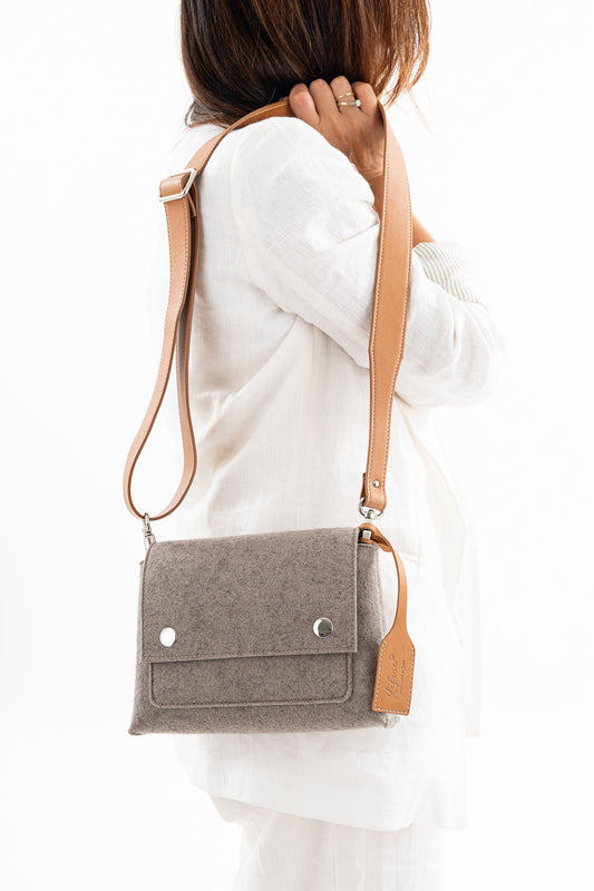 JOY Taupe Crossbody Bag, crafted from 3mm Merino wool felt and bio-based vegan leather. Features three pockets (2 external, 1 internal), flap closure with magnetic buttons, and an adjustable strap. Handmade in Italy with durability and eco-friendly qualities. Comes with a dust bag.